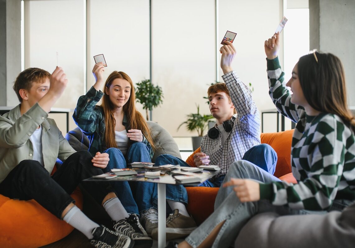 Four cheerful young adults enjoying their leisure time, playing cards sitting on beanbag chairs in a modern apartment SSUCv3H4sIAAAAAAAACpxTy4rcMBC8B/IPg88rkKx3fiXk0JJaOyIea7DlDcuy/x75NWgCIZCbu7qqH+ryx9cvl0vnYE6++3b5WKMap2FY5jJBSXmsMH058AnHgFOLvE1c0RaA1EYYUslTgqEFHRR/HeGGFRyXYVjhzy3ZzQXKMuPczBImhNtc0kbnDddDwdda/Il9bvJ9jy9nYktWRU113UuDzYvbsBPai/+Xcv/48XiJVxz9+zrbZzP1hAPCvuExY8ddj0owQYQxloigJbG+54RGZXoflVUWz86doNoypoEA61eyjMQJMKQPDJWJPXdBPMg2Gu8cVURyR4lwkhNLWZVFZ0IEb7U0D7LuIXKMQLgIgQjvkdgQkGiHgOAiWi+3ZfcNu5+/Ck637fGP3WAJKTfHeMsehvmPs0G6wwRPuvuUfBpfGySX6+azs5LPy1im9/YG3ZDzHdyw2iLWNnjiV5jnSg8n3lqmujrfmj5jLtspjqpdqJ5aQ8YF5ZpSaZSRsldMH4TdoNdU62zjnAMu9yFDwLXpwzfP1mVa2p4ZLsWeP422+uiWSvmntldG2EP79Mtk/zOFv/4y1TFK13002453qNLarRPoQNtACcft5IIR6zQSNJTHoHhPZaiqz98AAAD//wMAhPe4ByYEAAA=